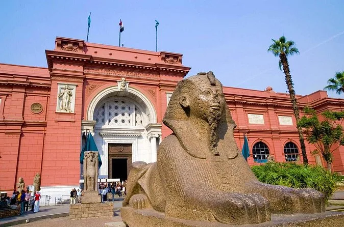 A granite sphinx in front of the arched entrance of the Egyptian Museum on a sunny day