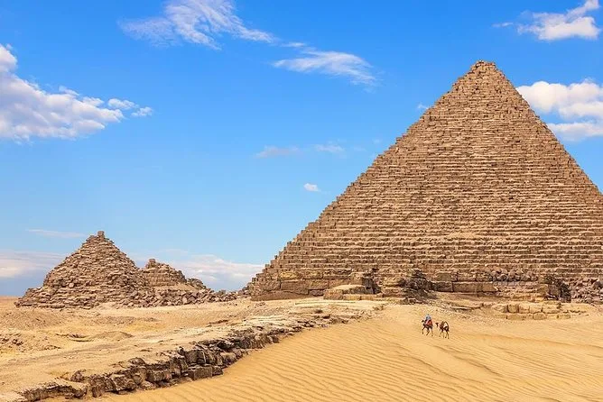 The Great Pyramid of Giza and smaller pyramids under a blue sky, with a road across the sand