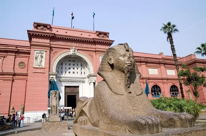 The salmon-red facade of the Egyptian Museum with a granite sphinx in the front garden
