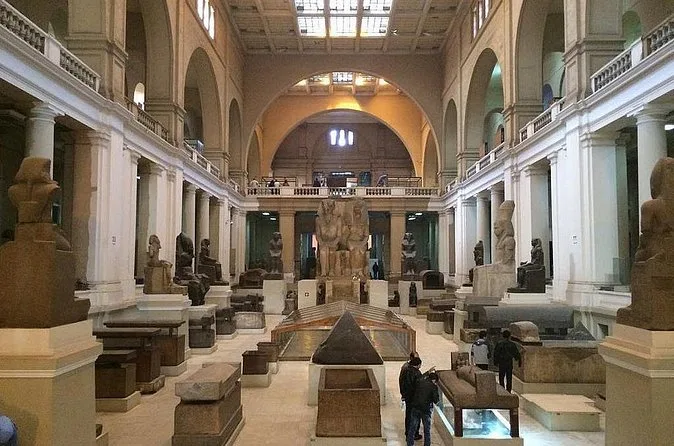 A long ground-floor hall of the Egyptian Museum with stone statues and sarcophagi under a glass roof